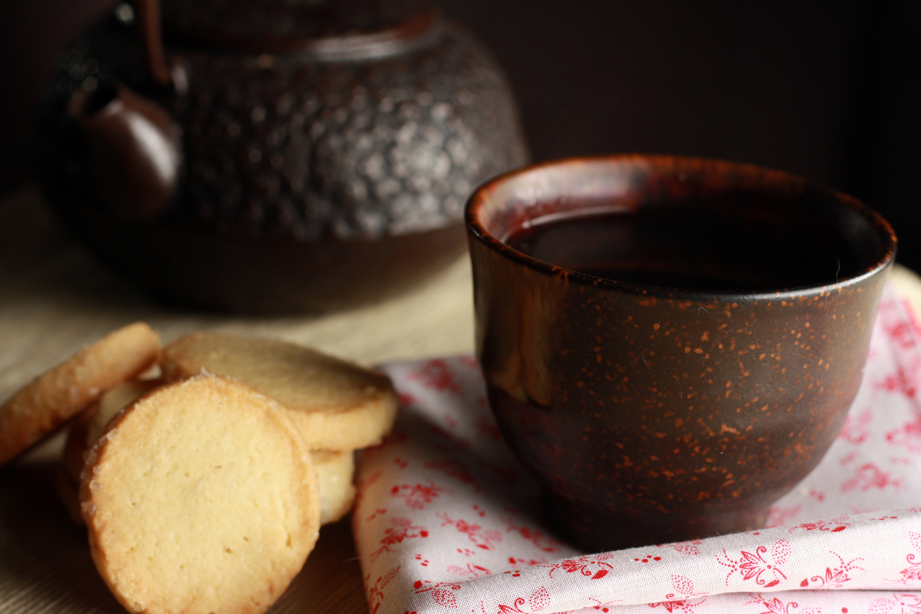 Butter cookies and a tea cup sit in the foreground with a cast iron teapot in the background.